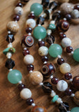 Close up view of 8mm and 6mm Picture Jasper (light brown with dark brown specks, dots, and lines); 8mm red and light brown Dzi Agate beads; light green Adventurine; Turquoise chip beads framed with ivory seed beads; 6mm White African Opals framed with 4mm red Garnets. Vanilla cream knots between the beads protect and showcase the beautiful beads in this one-of-a-kind design.