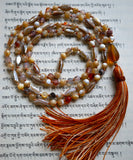 Full view of mala with Mother-of-Pearl, Shell, and Dendritic Agate beads in muted hues of cream, white, oyster gray, orange, and brown. The teardrop shaped sea glass guru brings this design full circle. A variegated tassel spills from the base of the guru.