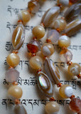 Close up view of rice-shaped shell beads with white, cream, and oyster gray swirls. 6mm faceted Dendritic Agate with white, gray, and orange variations. 6mm cream and white Mother-of-Pearl beads. Variegated brown knots between each bead protect and showcase the beads.