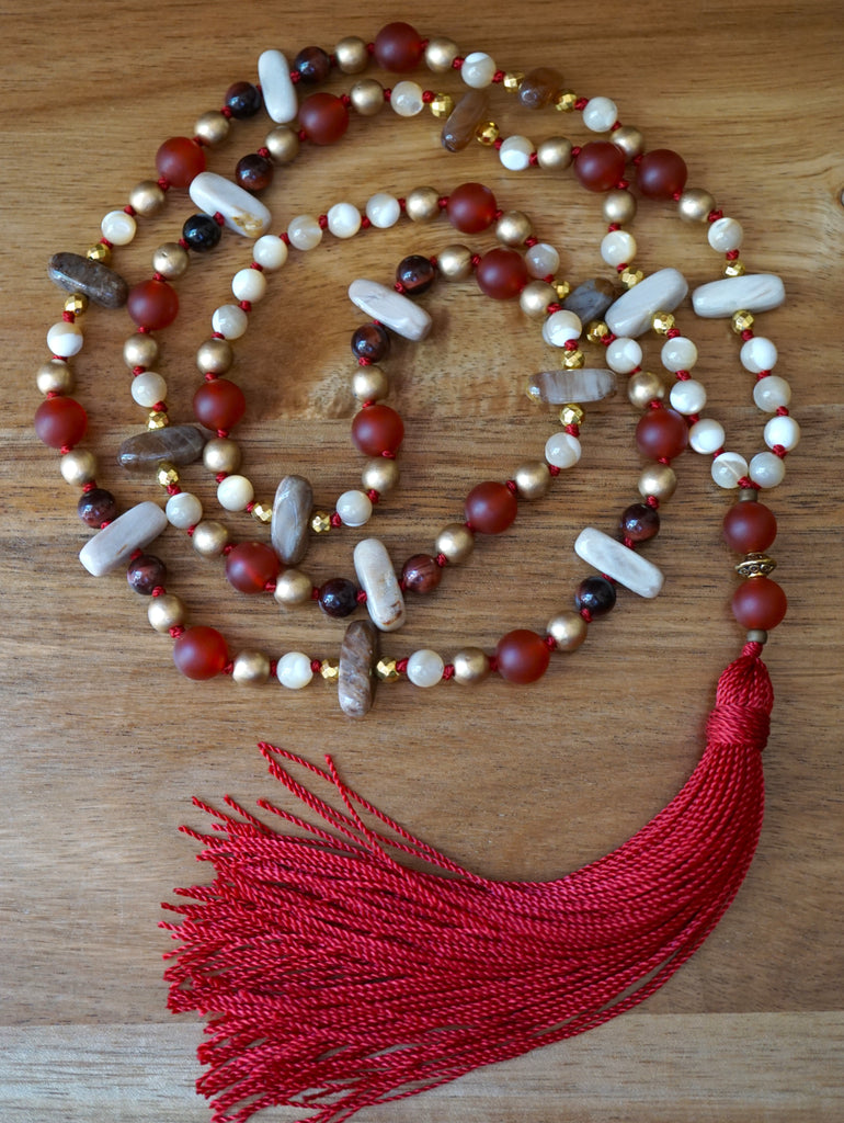 Full view of mala with 6mm light and dark cream Mother of Pearl beads, 6mm brushed gold Czech glass beads, 6mm Red Tiger Eye beads, 5x15mm center drilled light and dark brown Wood Opalite flat chip beads, 8mm matte Carnelian beads with double Carnelian guru separated by a gold spacer bead and deep red sutra and tassel.