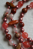 Close up view of Red Porcelain Jasper beads (round and flat chip) with warm rust, blush, wine, pink, and mauve tones; 8mm dark pink Cherry Quartz; 6mm light pink faceted Rose Quartz, and copper Czech glass beads. Salmon pink knots between beads protect and showcase the beads of this design.