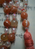 Close up view of guru-- 8mm double Red Botswana Agate beads separated by pearlescent seed beads. A salmon colored tassel brings this design full circle.