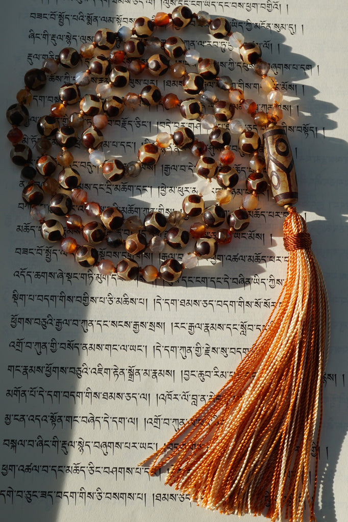Full view of Turtle Agate Mala with 8mm Turtle Agate beads , light brown, opaque beads with dark brown "shell-like" designs and 6mm starcut Madagascar Dendritic Agate beads, opaque stones in shades of milky white, orange, yellow, brown and gray. The Six-Eye Dzi Agate guru brings this design full circle with a variegated brown tassel spilling from the base of the bead.