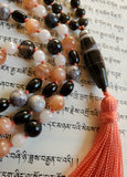 Close up view of 8x40mm Sardonyx guru with peach tassel spilling from the base of this bead.
