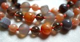 Close up view of bright Orange Agate, translucent brown Smoky Quartz, soft Peach Moonstone, gray Botswana agate (rounds and spiral cut), and matte gray Chalcedony beads. The soft peach knots between the beads protect and showcase the beads of this design beautifully.