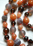 Close up view of bright orange Banded Agate, light Peach Moonstone, matte Gray Chalcedony, Spiral cut Botswana Agate, and translucent brown Smoky Quartz beads. The soft peach knots between the beads help protect and showcase the beads in this one-of-a-kind mala design.