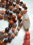 Close up view of a barrel-shaped, spiral-cut white Chalcedony guru with a flash of orange to complement the beads of this design. A soft peach tassel spills from the base of this guru, bringing this mala full circle.