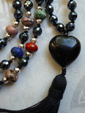 Close up view of  12x24mm heart-shaped Obsidian guru with black tassel spilling from the base of the bead.