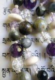 Close up view of cream-colored Pine rondelles framed with 4mm faceted Lavender Amethyst; 6mm and 8mm gray Cat's Eye beads, 8mm faceted Purple Amethyst, and 6mm Crackle Quartz beads. Cream-colored knots between the beads showcase and protect the beads of this design beautifully.