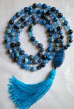 Full view of mala with dark blue Azure Agate beads with blue whorls and bands. Faceted light blue Aqua Jade beads. Oval Blue Crazy Lace Agate guru with bands and striations and parrot-blue tassel. This hand-knotted mala is a one-of-a-kind mala design.