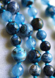 Close up view of 8mm and 6mm Azure Agate beads with various whorls and bands in the beads. 6mm light blue Aqua Jade beads add texture and shine to this design. The parrot-blue knots between beads showcase and protect the beads of this design beautifully.