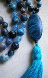 Close up view of 15x30 mm oval Blue Crazy Lace Agate guru. Known as the stone of laughter, it brings this design full circle. A parrot-blue tassel spills from the base of this focal bead.
