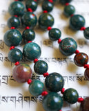 Close up view of green Dragon Blood Jasper beads separated by deep red knots that protect and showcase the beads of this powerful design.