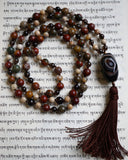 Full view of mala with transparent brown Smoky Quartz; red, gray, and brown Red Creek Jasper; cream-colored White African Opal beads; a faceted barrel-shaped Brown Agate guru and chocolate brown sutra and tassel.
