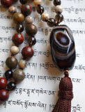 Close up view of faceted Brown Agate guru with white concentric circles. A chocolate brown tassel spills from the base of this focal bead.
