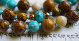 Close up view of faceted Aqua Impression Jasper rondelle bead framed with 4mm Czech glass beads, marking the quarter mark of this hand-knotted design.