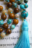 Close up view of 15mm round Aqua Impression Jasper guru with brown and tan inclusions. A sky blue tassel spills from the base of this focal bead.