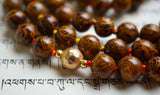 Close up view of 8mm brown Elephant Jasper beads with dark brown inclusions that resemble elephant skin. A textured gold metal bead marks the quarter point of this design. and colorful variegated knots protect and showcase the beads in this mala design.