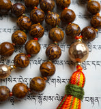 Close up view of the 12mm textured gold metal guru with a festive, variegated tassel spilling from the base of the bead, adding warmth and visual interest to this earthy mala design.
