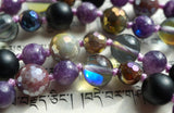 Close up view of faceted Fancy Jasper, matte black Onyx, purple Lepidolite, and translucent Mystic Aura beads. The lilac knots between the beads protect and showcase the beads of this design beautifully.