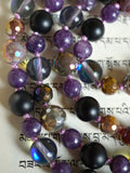 Close up view of rainbow-plated, faceted Fancy Jasper, translucent Mystic Aura, matte black Onyx, and purple Lepidolite beads. The lilac knots between the beads protect and showcase the beads of this mala design beautifully.