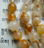 Close up view of 8mm and 6mm Golden Healer Quartz Beads. They range in color from white to soft yellow to golden brown. Honey gold knots between each bead protect and showcase the beads of this mala design.