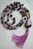This stunning mala includes dark green Seraphinite beads with featherlike inclusions, dark purple and lavender Amethyst, gray Agate, Quartz crystal, faceted Fancy Jasper, Porcelain Jasper, and an Ocean Jasper guru.