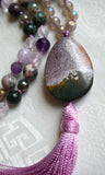 Close up view of 25x35mm Kabamby Ocean Jasper guru with purple, white, and dark green hues. A lavender tassel spills from the base of this bead, bringing this one-of-a-kind design full circle.