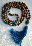 Full view of mala with an assortment of colorful Jasper and Agate beads: red, brown, yellow, green, blue, white. The oval Rainbow Calsilica guru with colorful bands of earthy hues: ochre, turquoise, deep green, white brings this design full circle, along with the marine blue tassel.