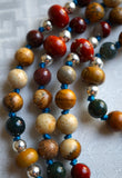 Close up view of earthy brown Picture Jasper, deep red Apple Jasper, green Fancy Jasper rounds and 8mm rondelle Red Jasper and Wood Jasper beads framed with 4mm silver Czech glass beads. The marine blue knots between protect and showcase the beads of this design.