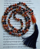 Full view of mala with 8mm Ancient Cellar Agate beads  in  swirling hues of brown, blue,  orange, and cream. 8mm banded Orange Agate; 6mm bright orange Fire Agate, and 6mm midnight Blue Goldstone with sparkly pyrite flecks. A stunning Orange Chalcedony guru brings this design full circle with navy blue tassel spilling from the base.
