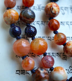 Close up view of 8mm Ancient Cellar Agate beads, 8mm banded Orange Agate, 6mm Fire Agate and Blue Goldstone beads. The navy blue knots between protect and showcase the beads of this one-of-a-kind design.