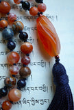 Close up view of 10x24mm barrel-shaped, spiral-cut Orange Chalcedony guru with a navy blue tassel spilling from the base of the focal bead.