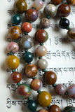 Close up view of Kabamby Ocean Jasper beads. Each bead is unique with dark green, mustard yellow, red, white, and brown colors. Deep sea green knots between the beads protect and showcase the beads of this hand-knotted design.