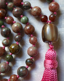 Close up view of 10x14mm barrel-shaped guru. Brown and cream striped resin with mauve tassel spilling from the base of the bead.  