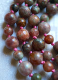 Close up view of 8mm and 6mm Kashgar Garnet beads. A blend of rose, pink, and green hues. Mauve knots between beads helps protect and showcase the beads in this mala design.