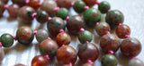 Kashgar Garnet beads are a blend of rose, pink, and green hues. Mauve knots between the beads help protect and showcase the beads of this one-of-a-kind design.