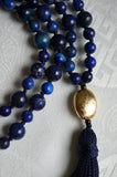 Close up view of oval, textured gold metal guru and navy-blue tassel which spills from the base of this focal bead.