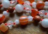 close up view of Orange Agate bead framed with 4mm white Moonstone; 6mm Goldstone with flecks of copper; 6mm star-cut Quartz; 8x13mm Orange chalcedony chip beads add texture and visual interest to this hand-knotted design.