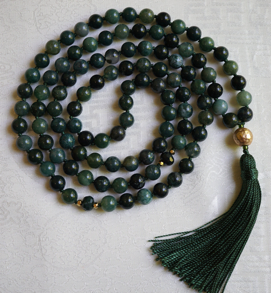 Full view of mala with 8mm deep forest green  Moss Agate beads, two faceted rondelles framed with 4mm gold metal mark the quarter and three-quarter marks of this design. A 12mm textured gold metal guru brings this design full circle. A forest green tassel spills from the base of the guru.
