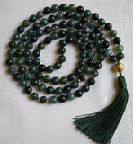 Full view of mala with 8mm deep forest green  Moss Agate beads, two faceted rondelles framed with 4mm gold metal mark the quarter and three-quarter marks of this design. A 12mm textured gold metal guru brings this design full circle. A forest green tassel spills from the base of the guru.
