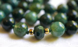 Close up view of 8mm faceted rondelle Moss Agate bead framed with 4mm gold metal beads. This bead marks the quarter mark of the mala. A matching bead unit marks the three-quarter mark of this mala design.
