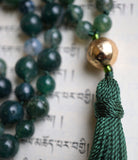 Close up view of 12mm textured gold metal guru and forest green tassel that spills from the base of this focal bead.