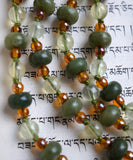 Close up view of light green Prehnite beads, dark green Olivine Jade rondelles framed with 4mm translucent topaz Czech glass beads. Olive green knots between the beads and bead units protect and showcase the beads of this mala design.