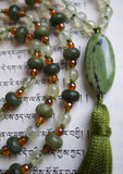 Close up view of 15x30mm oval Jade guru with olive green tassel spilling from the base of this hand-knotted mala design.