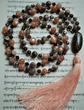Full view of mala. 8mm Peach Moonstone, 6mm faceted and round  brown Smoky Quartz beads combine with 15x30mm oval Red Creek Jasper guru and light peach sutra and tassel. This mala is hand-knotted and one-of-a-kind.