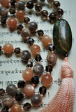 Close up view of 15x30mm oval Red Creek Jasper guru (brown, gray, with cream colored inclusions). A beautiful focal that brings all the beads together. Light peach tassel spills from the base of the bead.