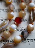 Close up view of 6mm faceted Dendritic Agate, 6mm cream and white Mother-of-Pearl, and rice shaped shell beads in white, cream, and oyster grey. Variegated brown knots between the beads protect and showcase the beads in this design.
