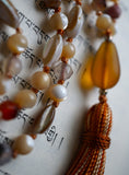 Close up view of amber colored sea glass guru. The teardrop shape adds visual interest and elegance to this design. A variegated brown tassel spills from the base of this focal bead.