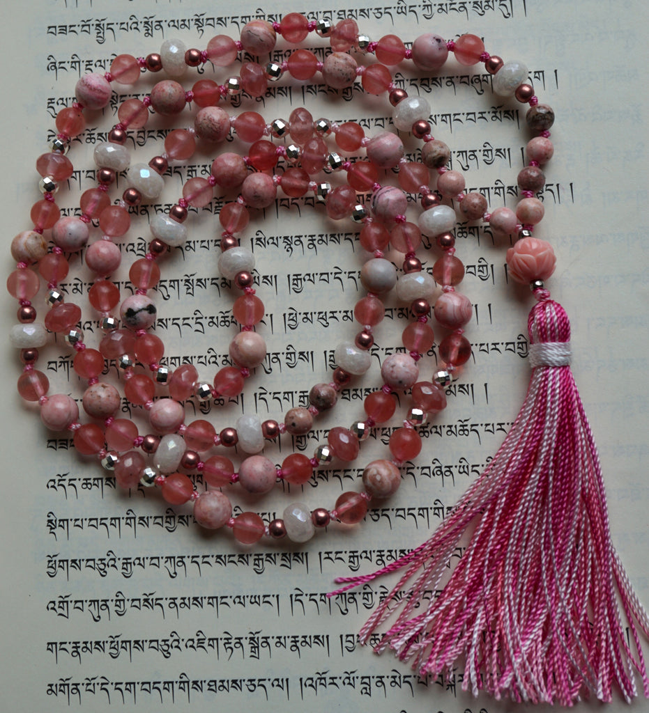Full view of Pink Lotus mala. 8mm and 6mm pink Rhodochrosite rounds with bands of light brown, dark pink, and cream . Dark pink Cherry Quartz rondelles framed with 4mm faceted silver Czech glass beads; faceted White Agate rondelles framed with rose Czech glass beads; 12mm resin pink lotus guru with variegated pink tassel spilling from the base.